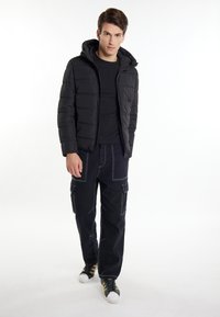 Jachetă căptușită neagră cu glugă, având cusături orizontale. Asortată cu pantaloni cargo închiși la culoare și adidași negri. Design simplu și funcțional.