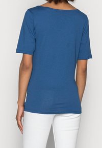 Maglietta blu a maniche corte realizzata in un tessuto liscio e leggero, con scollatura rotonda, design semplice e forma leggermente aderente.