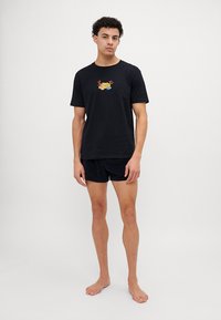 Schwarzes Baumwoll-T-Shirt mit kurzen Ärmeln und einem bunten, gestickten Design auf der Brust, kombiniert mit schwarzen Shorts.