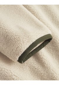 Krémové fleecové látky s jemným, textúrovaným povrchom; obsahuje tmavozelený lem pozdĺž okraja, ktorý poskytuje kontrast a detail.