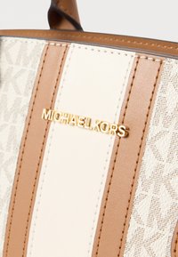 Καφέ δερμάτινη τσάντα χειρός με κρεμ κάθετες ρίγες και χρυσό λογότυπο με σήμανση. Υφασμάτινη επένδυση με υφή και διακριτικό σχέδιο.