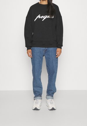 Sweatshirt noir avec le texte "peqas" blanc, associé à un jean bleu clair et des baskets grises. Tissu doux, coupe décontractée et poignets côtelés.