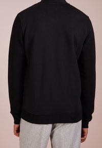 Felpa nera con finitura testurizzata, polsini e vita a costine. Presenta un colletto alto e un design senza cuciture sul retro.