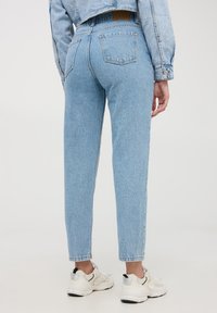 Jeans in denim azzurro chiaro con vita alta e gamba dritta, dotati di due tasche posteriori e un leggero sbiadimento. Indossati con sneaker bianche.