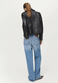 Zwarte cropped leren jas met ritssluitingen aan de manchetten, gecombineerd met lichtblauwe wijde jeans met achterzakken en een bruine patch op de tailleband.