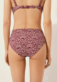 Bikiniunderdel i djup burgund med blommönster i ljuskräm. Hög midja, mjuk textur och sömlösa kanter. Justerbar stängning med remmar.