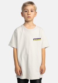 Svetle šedé bavlněné tričko s krátkým rukávem, kulatým výstřihem a logem DC Shoes v purpurové a žluté barvě na levé hrudi. Klasický střih.