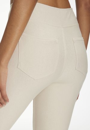 Beige hochtaillierte Leggings bestehen aus einem strukturierten Stoff, haben zwei Gesäßtaschen und ein eng anliegendes Design, das sich der Körperform anpasst.