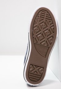 Semelle extérieure en caoutchouc marron de chaussures en toile bleu marine avec des accents blancs, présentant un motif de semelle en losanges et un logo "Converse All Star".