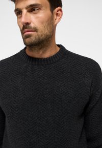 Dunkelgrauer Strickpullover mit einem strukturierten Fischgratmuster, geripptem Rundhalsausschnitt und weicher Textur. Nahaufnahme zur Hervorhebung der Designdetails.