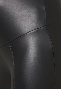 Svarta leggings i konstläder med en slät yta, figursydd design och synliga sömmar längs sömmarna, som framhäver en smal silhuett.
