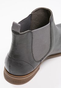 Gros plan sur l'arrière et le côté d'une botte Chelsea en cuir noir avec un panneau latéral élastique et une semelle marron.