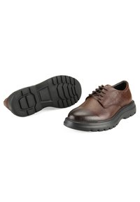 Bruine leren schoenen met een gestructureerde afwerking, vetersluiting en een dikke zwarte rubberen zool met een profiel voor grip.