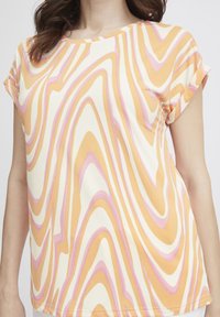 T-shirt med kortærmer med et bølgende mønster i gul, orange og pink på en cremefarvet baggrund; glat stof, afslappet pasform og rund halsudskæring.