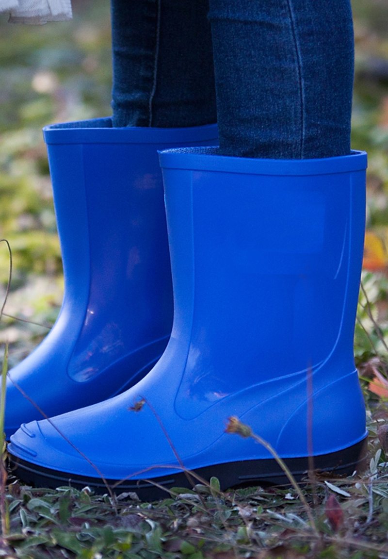 Jambes en bottes imperméables bleues debout sur de l'herbe et de petites plantes à l'extérieur.