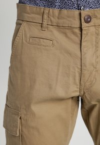 Khaki cargobroek van katoen, met meerdere zakken, een platte voorkant en een knoopsluiting. Soepele textuur met duurzame stitching.