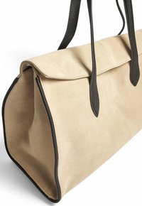 Borsa tote in suede beige con dettagli in pelle nera e tracolle in pelle nera, mostrata da un angolo laterale su uno sfondo bianco.