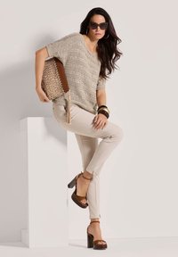 Beige gebreid top met korte mouwen, lichtbeige nauwsluitende broek, bruine platform hakken en een geweven handtas met een franje-detail.