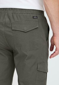 Grüne Cargo-Hosen verfügen über einen elastischen Bund, zwei Gesäßtaschen und eine Seitentasche mit Klappenverschluss. Das Material wirkt leicht und strapazierfähig.