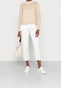 Felpa beige GAP indossata sopra una camicia bianca, abbinata a pantaloni bianchi corti e scarpe da ginnastica bianche. La borsa rosa chiaro aggiunge un tocco di contrasto.