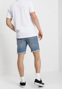 Biała koszulka z krótkim rękawem, jasnoniebieskie szorty dżinsowe z podwiniętymi nogawkami, czarne trampki i białe skarpetki, pokazane od tyłu.