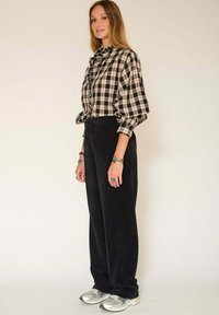 Chemise à carreaux à boutons avec des détails froncés, associée à un pantalon en velours côtelé noir. Des chaussures de sport argentées et des bracelets empilés viennent compléter le look.