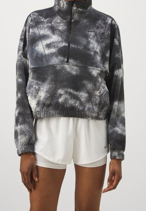 Person trägt ein schwarz-weißes Batik-Fleece-Halbzip-Sweatshirt und weiße Sportshorts mit elastischem Bund und Nike-Logo.