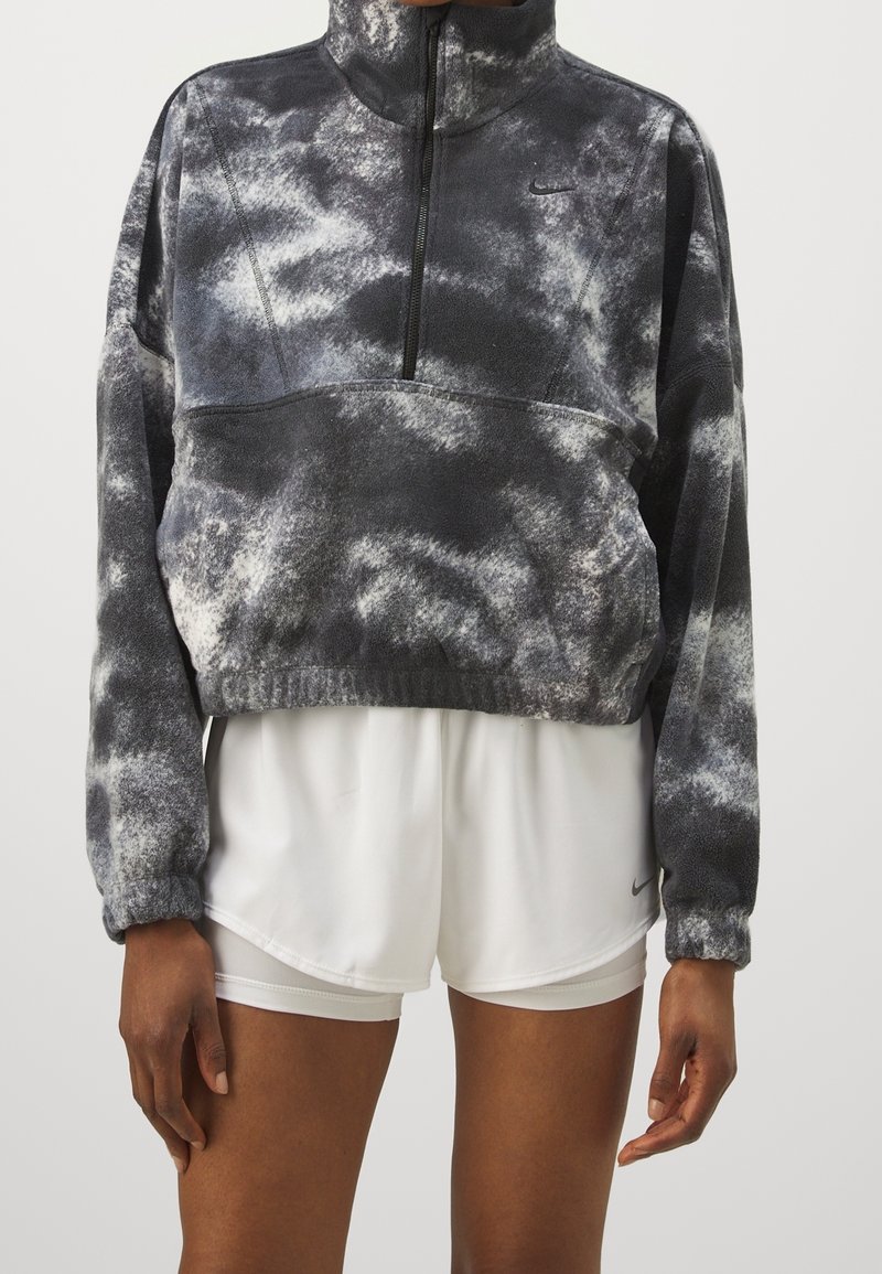 Personne portant un sweat polaire tie-dye noir et blanc à demi-fermeture éclair et un short de sport blanc avec taille élastique et logo Nike.