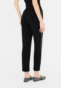 Zwarte taps toelopende sweatpants met een elastische tailleband, voorzien van een logo-detail aan de zijkant en opgerolde manchetten. Gladde stof met een lichte glans.