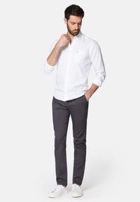 Biała koszula z długim rękawem i guzikami, z kieszenią na piersi, zestawiona z ciemnoszarymi spodniami slim fit i białymi trampkami. Prosty, czysty design.