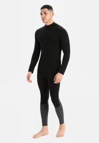 Fekete, hosszú ujjú felső, álló gallérral, fekete, testhezálló leggingsszel, az alsó részen szürke részletekkel. Simább textúra, sportos dizájn.