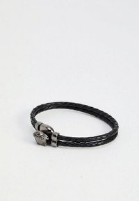 Črni pleteni usnjeni zapestnica s srebrno zaponko v obliki lobanje na belem ozadju