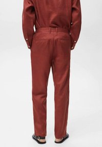 Rust-colored trousers made of a smooth fabric with a slim fit, featuring back pockets and a standard waistband.
