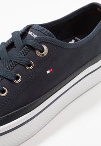 Marinblå canvas sneaker med metalöglor, vit gummisula och logodetalj. Har platta snören och en texturerad sidopaneldesign.