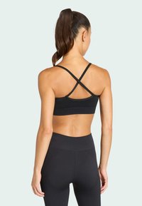 Μαύρο αθλητικό σουτιέν με διασταυρούμενες τιράντες στην πλάτη, διαθέτοντας λεία υφή και εφαρμοστό σχέδιο, συνδυασμένο με μαύρες κολάν ψηλής μέσης.