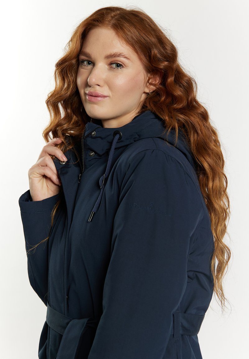 Dunkelblaue Steppjacke mit Kapuze, beltem Taillenbund, Reißverschluss und Druckknopfverschlüssen sowie Logodetail am Ärmel. Weiche Textur.