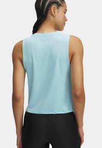 Lichtblauwe mouwloze crop top gemaakt van gladde stof. Heeft een ronde halslijn en een eenvoudig ontwerp. Zwarte leggings zijn zichtbaar eronder.