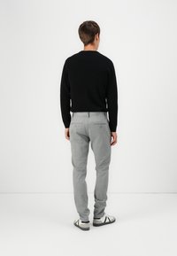 Suéter de punto negro, pantalones a rayas grises y zapatillas blancas. El conjunto presenta un diseño ajustado y una tela texturizada con costuras visibles.