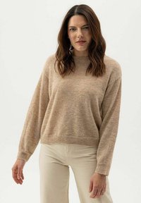 Beige kötött pulóver, kerek nyakkivág�ással, eső vállakkal és hosszú ujjakkal. Puha tapintás és laza fazon, világos színű nadrággal párosítva.