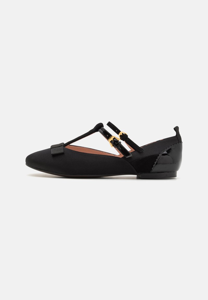 Black flat shoes with a smooth fabric upper, featuring two black straps with gold hardware and a small bow detail at the front.