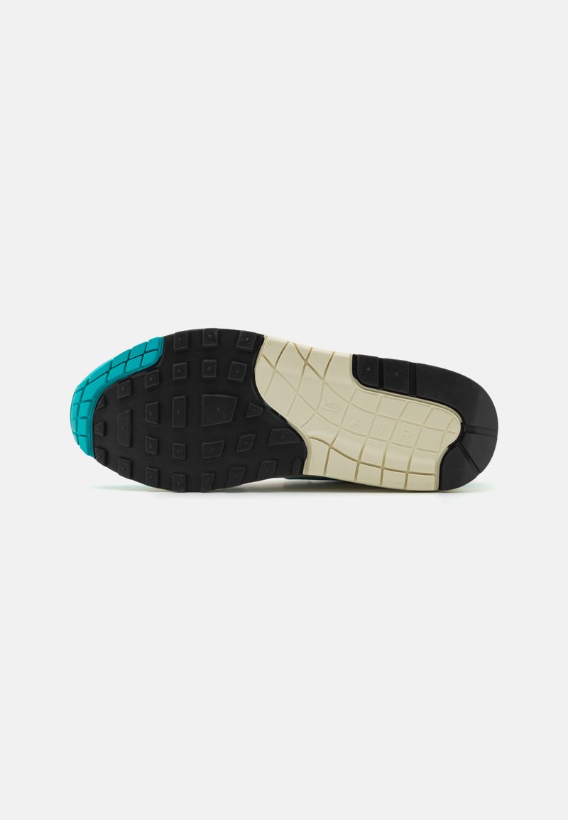 Zwarte zool met gestructureerd patroon, lichtbeige tussenzool en teal-accenten bij de teen. Ontworpen voor grip en comfort.