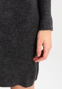 Robe-pull en laine gris charbon avec manches longues, texture côtelée, fentes latérales à l'ourlet et finition douce et duveteuse près des poignets.