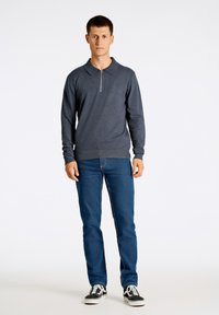 Tummanharmaa pitkähihainen polo, jossa on vetoketju, yhdistettynä sinisiin farkkuihin ja mustiin lenkkareihin, joissa on valkoisia yksityiskohtia. Yksivärisiä, minimalistinen muotoilu.