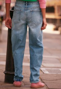 Jeans de mezclilla azul claro con un corte relajado, que cuentan con dos bolsillos traseros y una cintura, combinados con zapatos rosas y una superficie texturizada.