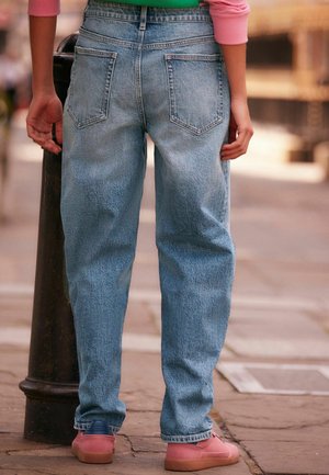 Heled sinine denim püksid, millel on relaxed fit, kaks tagumist taskut ja vöökoht, kombineeritud roosade kingadega ja tekstureeritud pinnaga.