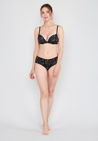 Zwarte beha en bijpassende slip met een subtiel gouden gemarmerd patroon. De beha heeft een diepe decolleté en verstelbare bandjes.