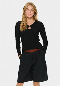 Black ribbed knit long-sleeve top with a keyhole neckline detail. Paired with high-waisted black shorts and a brown leather belt.