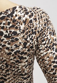 Brązowa i czarna bluzka w zwierzęcy wzór wykonana z elastycznego materiału, charakteryzująca się okrągłym dekoltem i krótkimi rękawami, podkreślająca teksturowany wzór.