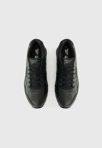 Zwarte sportieve schoenen met een glad leren bovenwerk en geperforeerde neus. Dikke zwarte veters en een gestructureerde rubberen zool. Reebok-logo op de tong.