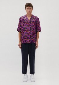 Camicia a maniche corte con bottoni di colore viola con una stampa a leopardo audace. Indossata con pantaloni scuri e sneakers bianche.